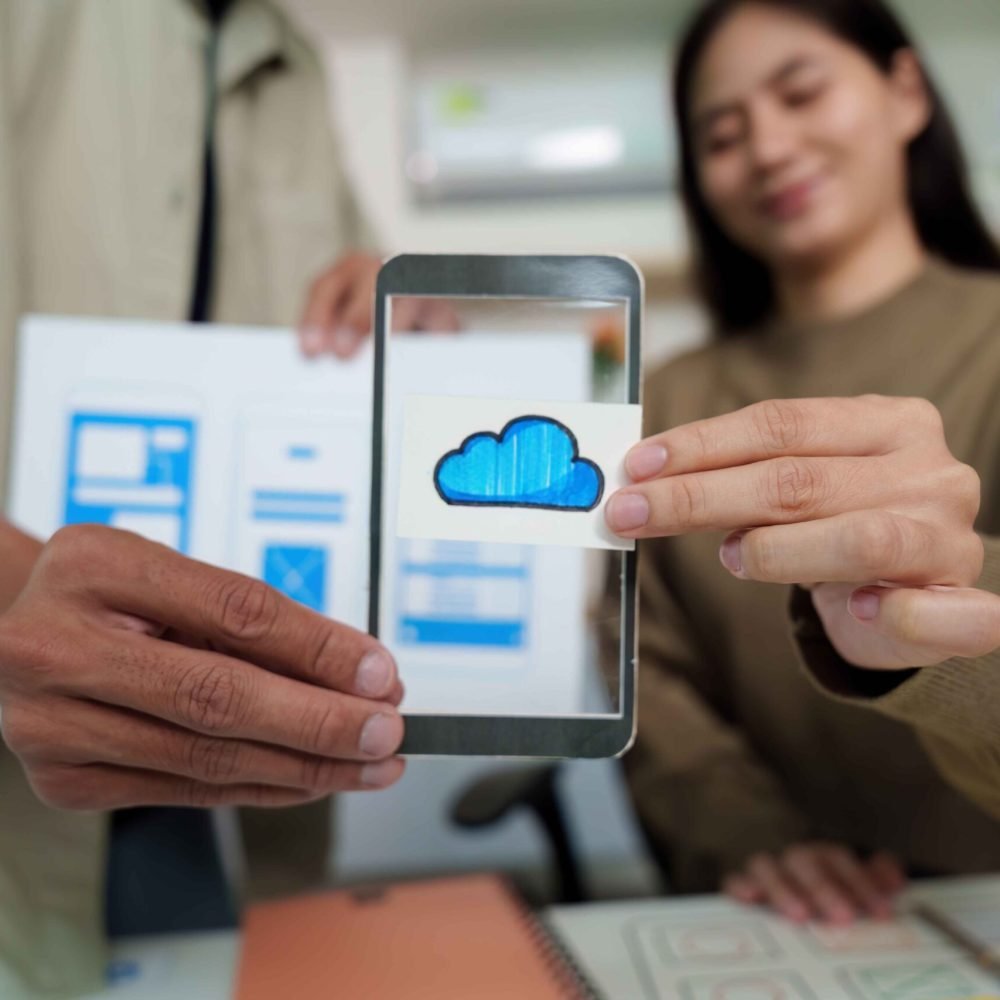 Designers presenting cloud technology features on a mobile device during a UI/UX design session, highlighting innovation and teamwork.